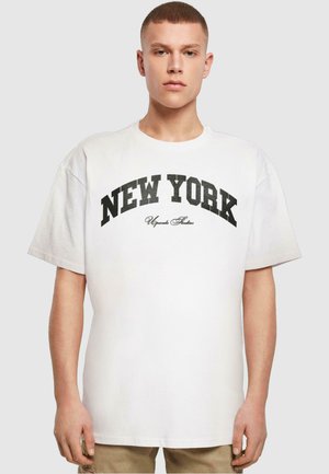 Hvid bomulds t-shirt med en afslappet pasform, der har et sort "NEW YORK" print og "Upgrade Studios" i kursiv nedenunder. Blød tekstur og korte ærmer.