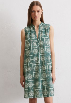 Sleeveless dress in green fabric featuring a geometric white print. Design has a v-neckline and is knee-length with a relaxed fit.