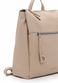 Kreminkrāsas ādas rokassoma ar strukturētu virsmu, kurai ir rāvējslēdzēja augšpuse, priekšējais kabata un cilpas roktura akcenti.