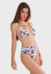 Bikini set s barevnými abstraktními vzory na bílém pozadí. Obsahuje trojúhelníkovou podprsenku a šortky s vysokým pasem pro větší zakrytí.
