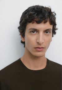 Braunes T-Shirt mit Rundhalsausschnitt, glatter Stoff, eng anliegendes Design, einfarbige Textur. Modell hat lockiges dunkles Haar und neutralen Hintergrund.