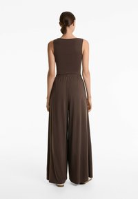 Une combinaison brune avec un haut sans manches ajusté et un pantalon large, dotée d'une taille élastique et d'une texture lisse.