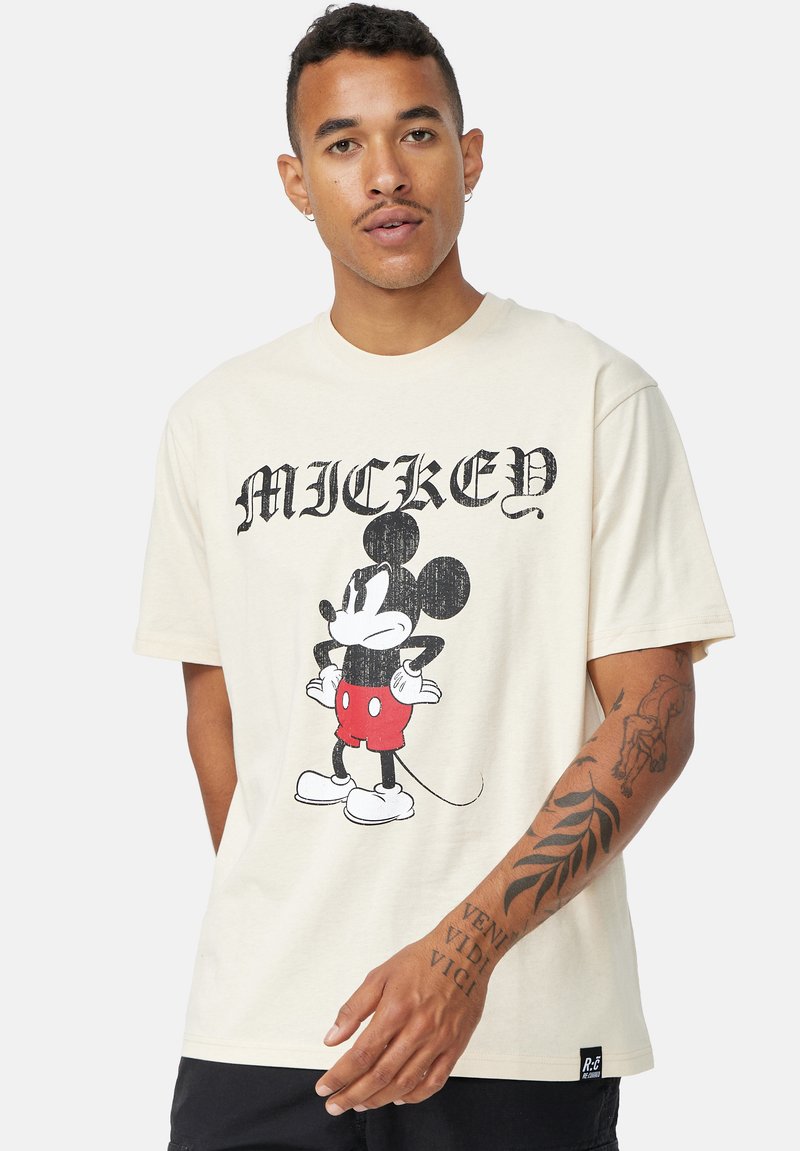 Camiseta de algodón beige con un gráfico de estilo vintage de Mickey Mouse en pantalones cortos rojos. Manga corta y corte relajado. Etiqueta de logo negra en el dobladillo.