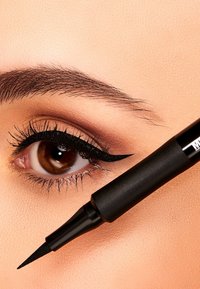 Una penna per eyeliner liquido nero presenta un applicatore a punta fine. Primo piano di un occhio con eyeliner a punta definita e ciglia voluminose.