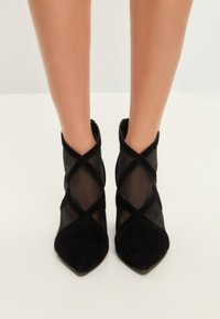 Stivaletti neri alla caviglia in una combinazione di morbido suede e rete trasparente, con punta affusolata e elementi di design a incrocio.