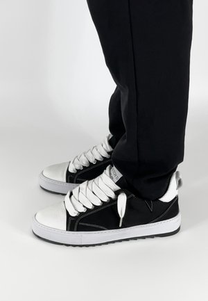 Zwart-witte sneakers met een glad leren neus, canvas bovenkant, witte veters en contrasterende stiksels. Geen zichtbare logo's of patronen.