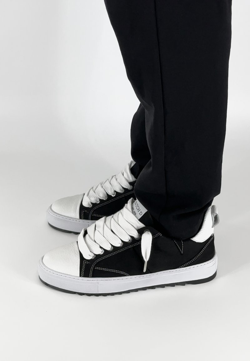 Zwart-witte sneakers met een glad leren neus, canvas bovenkant, witte veters en contrasterende stiksels. Geen zichtbare logo's of patronen.