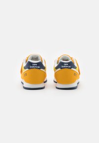 Žluté a šedé tenisky New Balance 373 s texturovaným svrškem, bílou mezipodešví a námořnickou modrou podrážkou. Číslo "373" na patě.