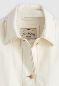 Crèmekleurige overhemdkraag met zichtbare stiksels, een knoopsluiting en een Levi Strauss-label met een kenmerkend ontwerp.