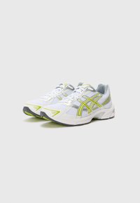 Sapatilhas brancas desportivas com parte superior em malha, pormenores em prata e detalhes em amarelo fluorescente. Possui uma sola acolchoada e um design de bico redondo.