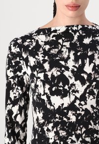 Langarmkleid mit einem schwarz-weißen abstrakten Muster, glatter Textur und einem Boot-Ausschnitt.