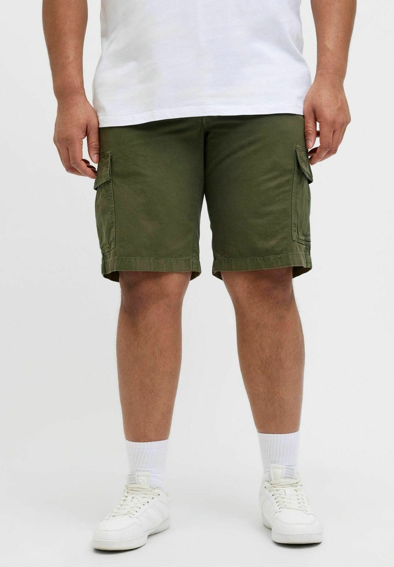 Bermudas cargo verde oliva con bolsillos laterales, hechas de un tejido duradero. Corte recto con un dobladillo justo por encima de la rodilla, combinadas con zapatillas blancas.