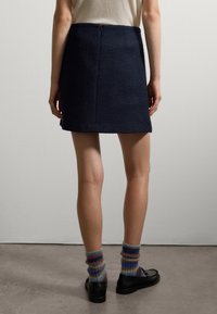 Gonna mini in navy con finitura testurizzata, chiusura con zip sul retro e spacchi laterali. Abbinata a calze a righe multicolori e mocassini neri.
