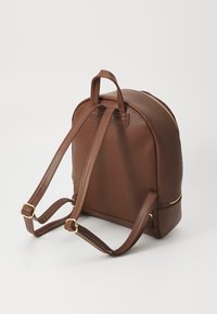 Sac à dos en faux cuir marron avec une forme arrondie, fermeture éclair dorée et bretelles ajustables. Comprend deux poignées supérieures et une texture lisse.