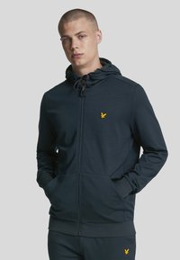 Dunkelblaues Reißverschluss-Hoodie aus weichem Material, mit einem gelben gestickten Logo auf der Brust, verstellbarem Kapuzen-über und Fronttaschen.
