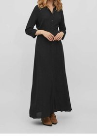 Dlouhá černá šaty vyrobená z lehkého materiálu s knoflíkovým zapínáním a dlouhými rukávy. Má uvolněný střih a délku až k kotníkům.