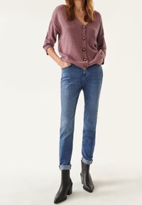 Svetr s V výstřihem, pohodlný fialový pletený cardigan s knoflíky, spárovaný s modrými denimovými džíny a černými jehlovými kotníkovými botami.