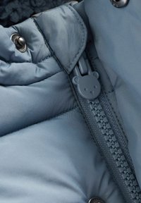 Hellblauer Daunenjackenbereich mit strukturierter Oberfläche, Druckknöpfen und einem Reißverschluss mit einem Bären-förmigen Zipper. Sanfte Fütterung innen sichtbar.