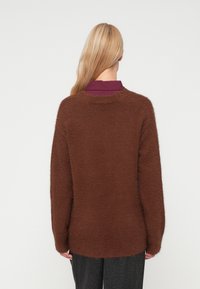 Sweater castanho fofo com decote redondo, ombros caídos e mangas longas. Material texturizado e suave com um corte largo.