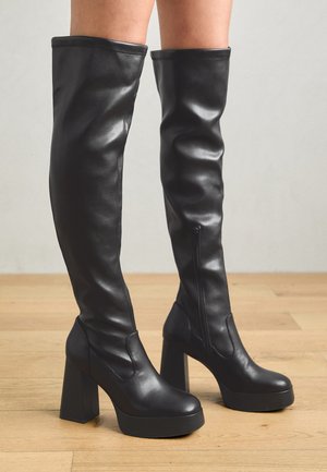 Bottes noires hautes en cuir lisse, avec une plateforme épaisse et un talon bloc ; dotées d'une fermeture éclair sur le côté et d'un design supérieur sans couture.