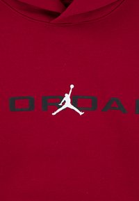 Červená mikina s kapucňou so bielym logom Jumpman a čiernym nápisom "ORDAN". Materiál vyzerá mäkko a má hladkú textúru.