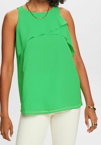 Top verde senza maniche con design a strati a volant, realizzato in un tessuto leggero con una superficie liscia. Collo rotondo semplice e vestibilità fluida.
