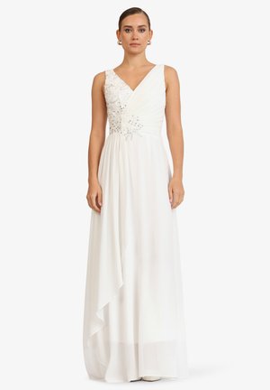 Woman wearing sleeveless white gown with beaded floral embellishments on bodice and pleated, flowing skirt against white background.