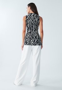 Mustvalge vabaajatuunika sebramustriga, paistab tagant vaates, kantud koos valgete lahtiste pükstega heleda taustaga.