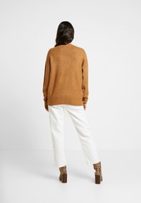 Brun stickad tröja med avslappnad passform, ribbade muddar och fåll, kombinerad med vita vida byxor och mönstrade högklackade stövlar.