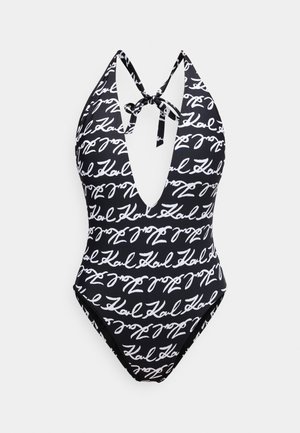 Fekete fürdőruha mély V-nyakkivágással és pántos megkötéssel, fehér, kézíráshoz hasonló mintával az egész felületen. Simább anyagból, testhez simuló szabással.