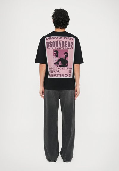 Maglietta nera unisex con una grande stampa grafica rosa sul retro con testo e immagini. Abbinata a jeans neri sbiaditi e ampi.