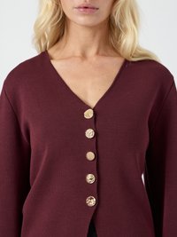 Burgundská pletená cardigan s výstrihom do V a šiestimi dekoratívnymi zlatými gombíkmi s detailnými vzormi na prednej strane. Textúrovaná tkanina.