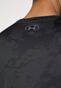 Μαύρο αθλητικό μπλουζάκι με υφή, διαθέτει στρογγυλή λαιμόκοψη και διακριτικό γκρι λογότυπο στην πλάτη κοντά στο ν γιακά.