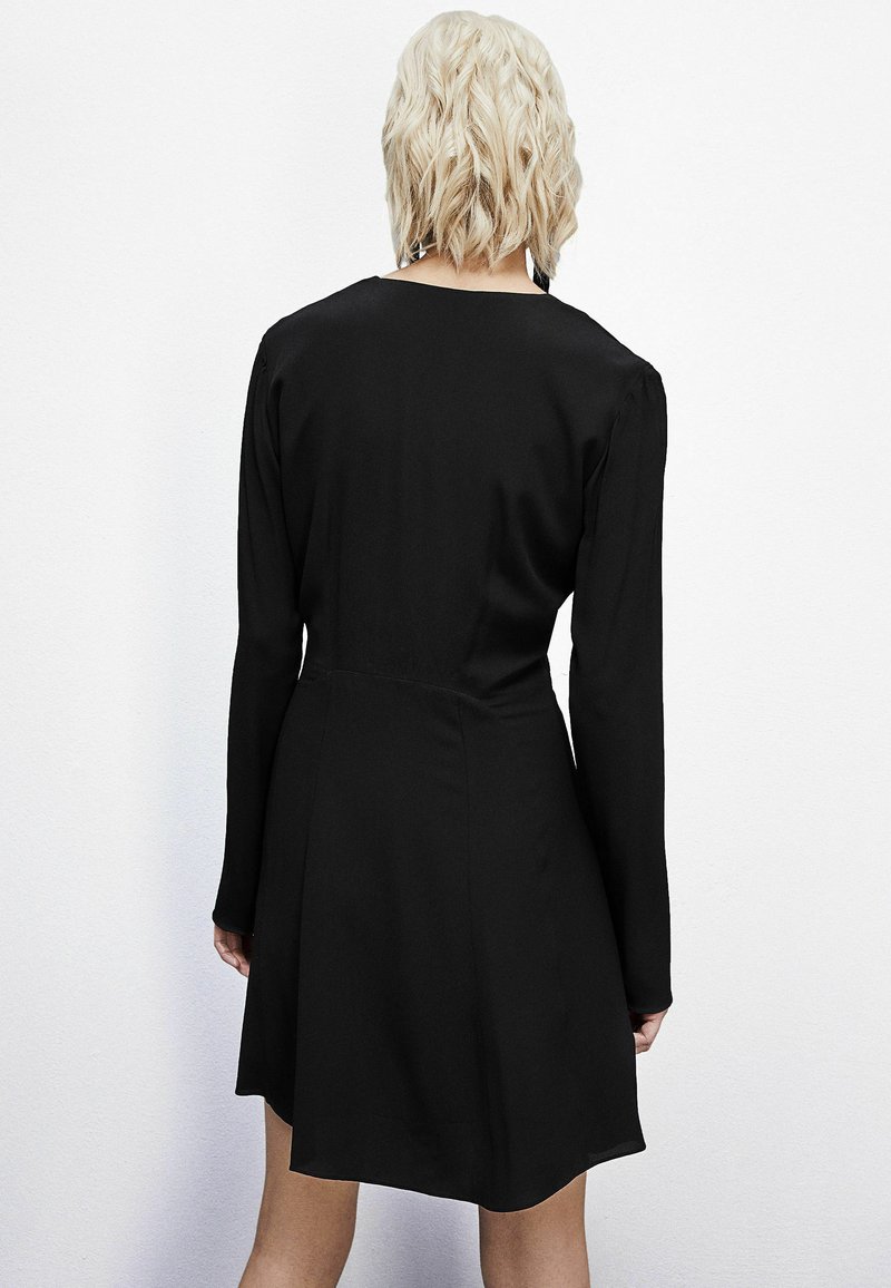 Schwarzes Kleid mit langen Ärmeln, einem runden Ausschnitt und einem taillierten Oberteil, das sich an der Taille ausweitet. Glatter Stoff mit einem schlichten Design.