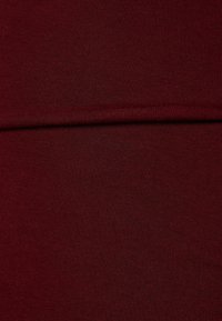 Burgundy bomullstyg, slät textur, ribbat mönster. Materialet visar en lätt glans under ljuset, med en jämn färg och yta.