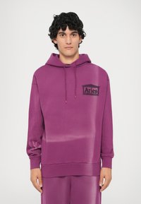 Hanorac violet din bumbac moale, cu buzunar frontal tip cangur, glugă cu șnur și un logo negru "Aries" pe piept, în partea stângă.