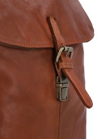 Zaino in pelle marrone con patta, dotato di chiusura a fibbia in metallo e dettagli cuciti, che mette in mostra una superficie testurizzata.