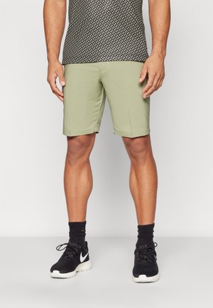 Light green athletic shorts with a smooth texture, side pockets, and a straight fit. Worn with black athletic shoes and socks.