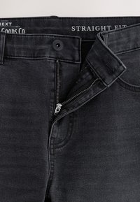 Dunkelgraue Jeans mit geradem Schnitt, teilweise offenem Reißverschluss und Knopfverschluss, sichtbaren Nähten und Vordertaschendetail.