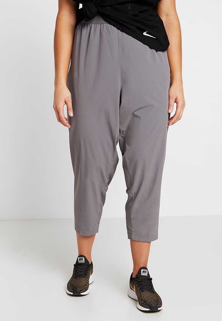 Pantalones grises recortados hechos de material ligero con un ajuste suelto y cintura elástica. Combinados con zapatillas deportivas negras con un diseño texturizado.