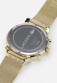 Montre en acier inoxydable doré avec un bracelet en maille, un boîtier rond et un cadran gris comportant un logo de marque gravé et des détails. Résistante à l'eau jusqu'à 5 bars.