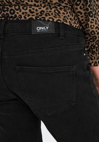 Des jeans en denim noir avec un design classique à cinq poches et un patch logo à l'arrière. Texture lisse avec une silhouette ajustée.