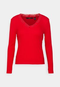 Punainen pitkähihainen paita, jossa on ribatttu pinta. Ominaisuuksiin kuuluu V-hihansuu, joka on koristeltu kukkaketjulla. Muotoon ommeltu malli ilman huomattavia yksityiskohtia.