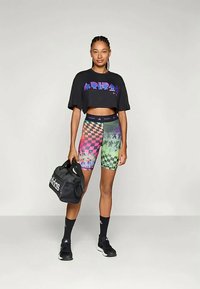 Must eksooni t-särk graafilise tekstiga, mitmevärvilised ruudulised kompressioonilühikesed püksid, mustad sokid ja must spordikott, seistes neutraalses taustas.