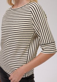 Striped knit top in cream with black horizontal lines. Features a round neckline, three-quarter sleeves, and a relaxed fit.