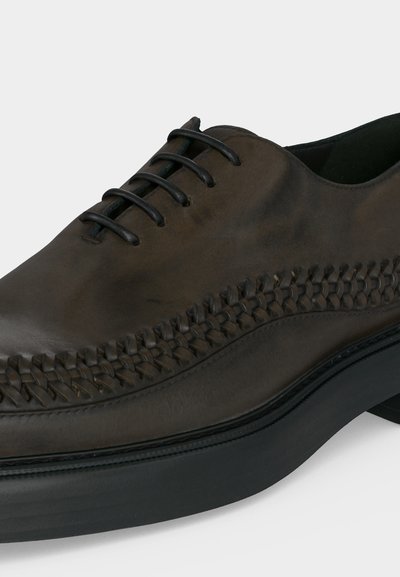 Σκούρο καφέ δερμάτινο παπούτσι με υφαντές λεπτομέρειες στο πλάι και μαύρα κορδόνια σε παχύ μαύρο πέλμα.