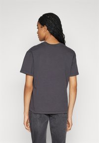 Γκρίζα βαμβακερή μπλούζα με κλασικό στρογγυλό λαιμό, κοντά μανίκια και άνετη γραμμή, εμφανιζόμενη από πίσω.