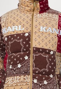 Gestepptes Daunenjacke mit einer Mischung aus braunen, beigen und roten Stoffen mit Bandana-Mustern. Goldener Reißverschluss und besticktes "KARL KANI"-Logo.