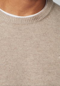 Beige knit sweater with a round neckline, featuring a textured ribbed pattern and subtle stitching details. Soft, lightweight fabric.