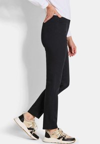 Zwarte rechte broek met een gladde textuur, gecombineerd met beige en zwarte sneakers met gaas- en stevige accenten.